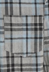Gros plan d'un tissu à carreaux gris, noir et bleu clair avec une poche carrée cousue dessus.