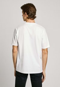 Vit bomull t-shirt med kort ärm, rund halsringning och en avslappnad passform. Bakifrån syns en jämn textur och enkel design.