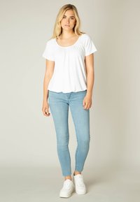 Witte top met korte mouwen en gathered halslijn, gecombineerd met lichtblauwe skinny jeans en witte platform sneakers. Glad textuur, casual pasvorm.