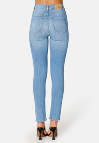 Jasnoniebieskie rurki z wysokim stanem, z dwoma tylnymi kieszeniami i brązową łatą ze skóry z tyłu. Noszone z czarnymi szpilkami.