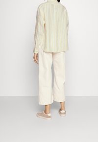 Yellow and white striped shirt with long sleeves, paired with cream wide-leg pants and beige sneakers, seen from the back.