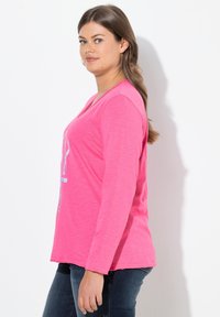 Långärmad rosa t-shirt i mjukt material, med en V-ringning och en grafisk design på framsidan. Slimmad, avslappnad passform.