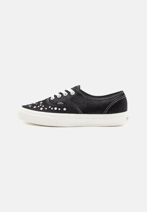 Black lace-up sneakers with a textured upper, featuring white rubber soles and decorative studding on the toe area. Distinct Vans branding.
