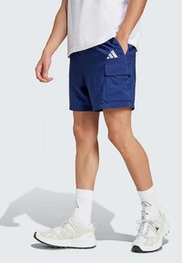 Tamsiai mėlynos šortai, pagaminti iš lengvos medžiagos, turi šoninį krovinių kišenę, mažą baltą logotipą ir reguliariai prigludusią formą. Derinami su baltais sportbačiais.