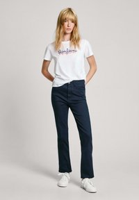 Bijela majica s višeobojenim logom "Pepe Jeans", uparena s tamnoplavim hlačama ravnog kroja i bijelim tenisicama. Jednostavna, ležerna kombinacija.
