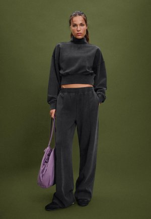 Sivý skrátený športový sveter s vysokým golierom, kombinovaný so zodpovedajúcimi voľnými teplákmi. Model nesie svetlofialovú tašku. Hladká štruktúrovaná tkanina.