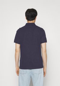 Marineblå polo med klassisk krage, kort ermer og ribbestrikkede mansjetter. Brukt med lyseblå denimjeans. Glatt bomullstekstur.
