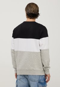 Bluza z okrągłym dekoltem z poziomymi pasami kolorów: czarny, biały i szary. Wykonana z mieszanki bawełny z prążkowanymi mankietami i dołem.