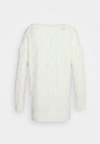 Jersey de punto blanco con un patrón de diamantes, pompones texturizados y puños y dobladillo acanalados. Diseñado con un escote amplio y mangas largas.