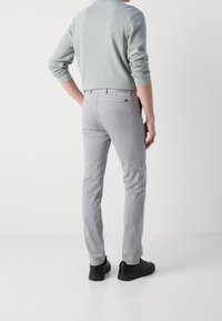 Szare wąskie spodnie wykonane z lekkiego materiału, z tylnymi kieszeniami, zestawione z jasnografitową bluzką z długim rękawem i czarnymi sneakersami.