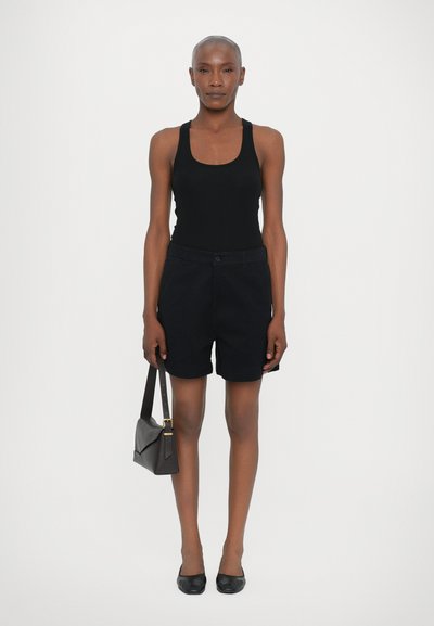 Svart tank topp kombinert med svarte shorts, akkompagnert av svarte leiligheter og en strukturert mørk veske med gullhardware.