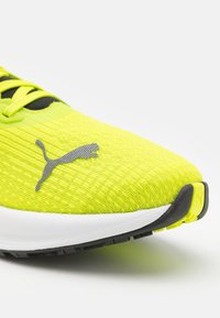 Zapatilla de running Puma con una parte superior texturizada en amarillo brillante, acentos negros y un logo gris. Cuenta con una entresuela blanca y una suela negra.