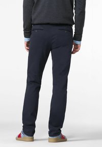 Marineblå bukser med slim fit, lavet af glat stof, med to baglommer med knapper, parret med røde og blå sneakers.