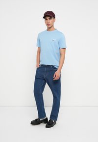 Tricou scurt cu mâneci ușoare de culoare albastru deschis, cu logo, asortat cu blugi relaxați de culoare albastru închis și mocasini negri, completat cu o șapcă maronie.