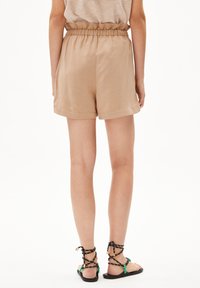 Licht beige, shorts met elastische taille met een gladde textuur. Gecombineerd met zwarte sandalen met groene accenten en gevlochten banden.