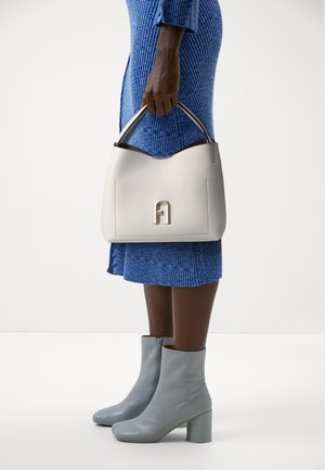 Witte leren handtas met een gestructureerde afwerking, gebogen bovenkant en opvallend logo detail. Gepaard met een blauwe geribde jurk en lichtblauwe enkellaarsjes.