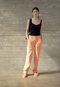 Top negro, pantalones cargo melocotón con bolsillos laterales y sandalias rosas. Diseño simple, corte holgado, material de algodón, hardware mínimo.