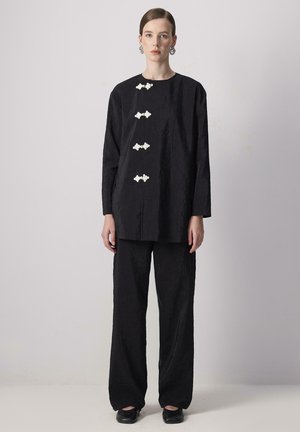 Un pantalon large noir et un haut surdimensionné présentant un tissu texturé, cinq boutons floraux blancs et des manches longues. Design simple et moderne.