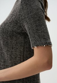 Abito grigio a scacchi con maniche corte, caratterizzato da polsini decorati. Silhouette strutturata con una finitura in tessuto testurizzato.