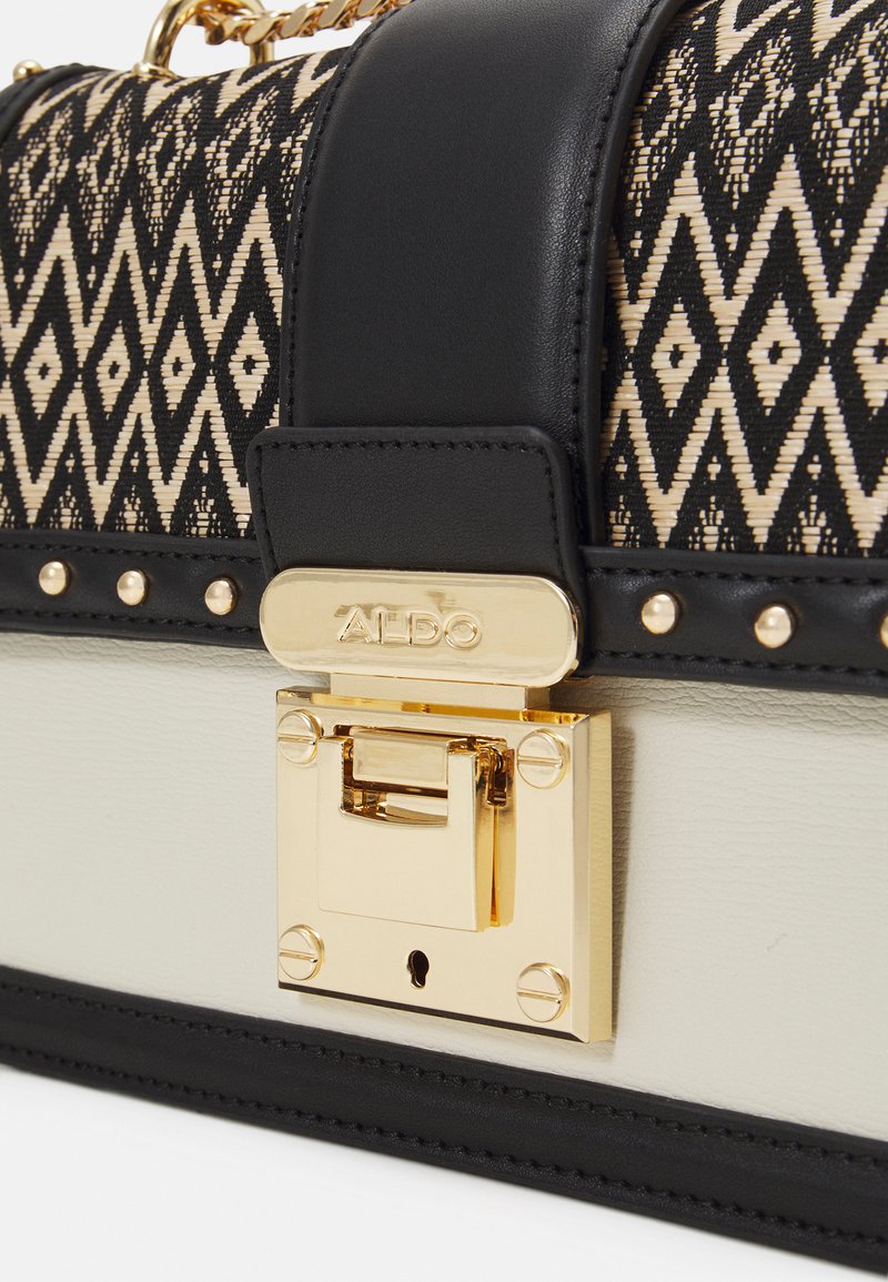 Sac à main noir et crème avec un motif tissé géométrique, fermoir en métal doré et accents cloutés ; combinaison de cuir lisse et de tissu texturé.