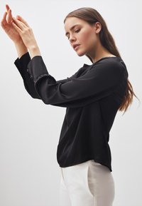 Blusa nera in satin con maniche lunghe e polsini abbottonati, caratterizzata da una texture morbida e liscia e da una vestibilità rilassata e favorevole.