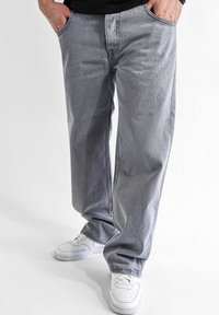 Light gray jeans with a straight-leg design, featuring a classic five-pocket style and subtle fading. Worn with white sneakers.
