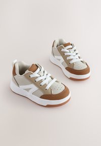 Baskets beige et marron clair avec des lacets blancs, un bout perforé et des semelles en caoutchouc. Comprend des accents marron et un col rembourré pour le confort.