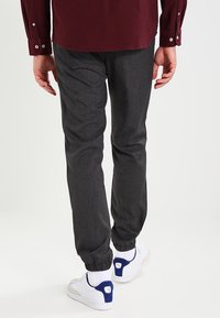 Persona che indossa pantaloni jogger grigio scuro, sneakers bianche con accenti blu e una maglietta a maniche lunghe bordeaux, vista da dietro.