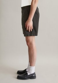 Heren donkergrijze shorts met een elastische tailleband, zijzakken en een rechte snit, gecombineerd met zwarte instappers en witte sokken.