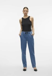 Crna bezrukavna majica s okruglim izrezom u kombinaciji s laganim plavim trapericama koje imaju elastičnu waistband i bočne džepove.