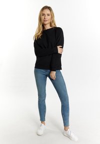 Maglione nero con scollo rotondo e maniche lunghe, abbinato a jeans skinny azzurri chiari e sneakers bianche. Tessuto liscio, vestibilità casual.