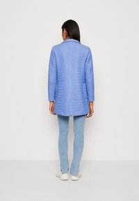 Abrigo azul claro con un diseño estructurado, mangas largas y dos bolsillos laterales. Tejido texturizado con un acabado suave, combinado con denim claro.