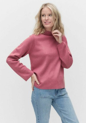 Ljust rosa, långärmad tröja med hög krage och avslappnad passform. Texturerad väv med sidofickor, kombinerad med blå jeans.
