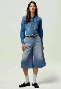 Chemise en denim avec col et fermeture à boutons, associée à un large pantalon culotte en denim. Couleur bleu clair, coupe décontractée et ceinture contrastante.