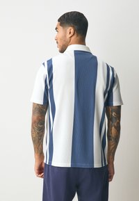 Kurzärmeliges Poloshirt mit vertikalen blau-weißen Streifen, gerippter Textur und flachem Kragen. Verfügt über eine lockere Passform und ein lässiges Design.