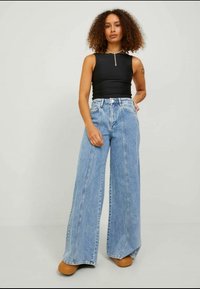 Breda ljusblå denimjeans med hög midja, med en lös passform, synlig sömnad och en slät yta. Kombineras med en åtsittande svart topp.