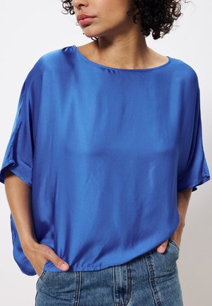 Top en satin bleu à manches courtes avec une coupe ample et un col rond. Assorti à un jean taille haute, mettant en valeur une texture lisse et un éclat.