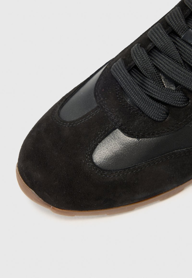 Sneaker noir avec une tige en daim et des accents en cuir lisse, une zone de lacet texturée et une semelle en caoutchouc.