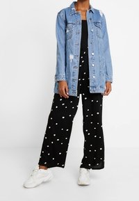 Světlě modrá džínová bunda s efekty opotřebení, kombinovaná s černými širokými kalhotami s bílými puntíky a bílými teniskami.