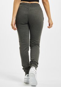 Joggers gris étroits avec une texture lisse et une taille élastique, associés à des baskets blanches avec un logo noir sur le côté.