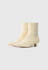 Bottines en cuir crème avec un bout pointu, un petit talon carré et une texture lisse, présentant un design sans couture pour une apparence élégante.