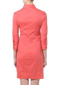 Korallinvärinen mekko, jossa istuva siluetti, kolmen neljänneksen hihat ja napit hihansuiden kohdalla. Sileää kangasta, klassinen kaulus ja selkäsauma.