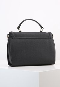 Svart strukturerad handväska med texturerat syntetiskt material, en övre handtag, magnetisk stängning och detaljer i silverfärgad metall.