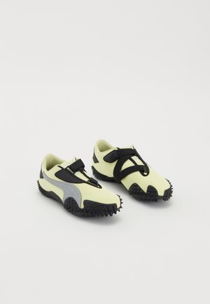 Paire de chaussures de sport jaunes et noires avec des semelles à crampons et des sangles noires ajustables sur fond blanc.