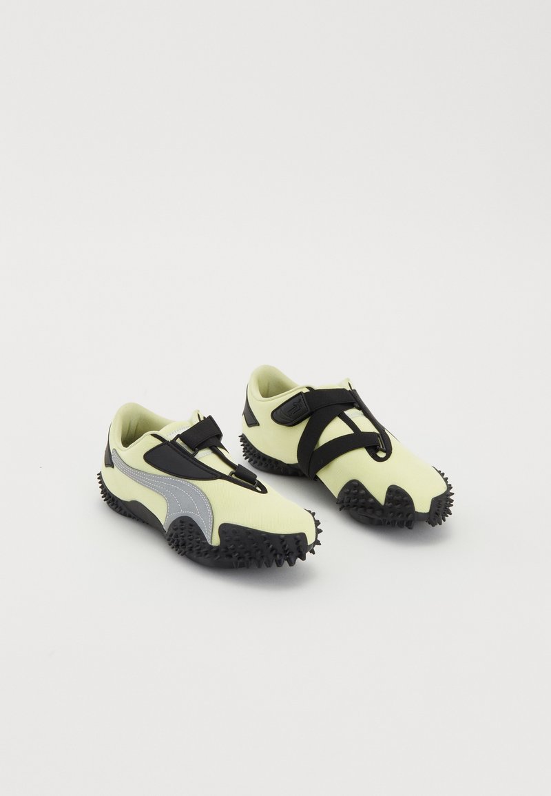 Paire de chaussures de sport jaunes et noires avec des semelles à crampons et des sangles noires ajustables sur fond blanc.