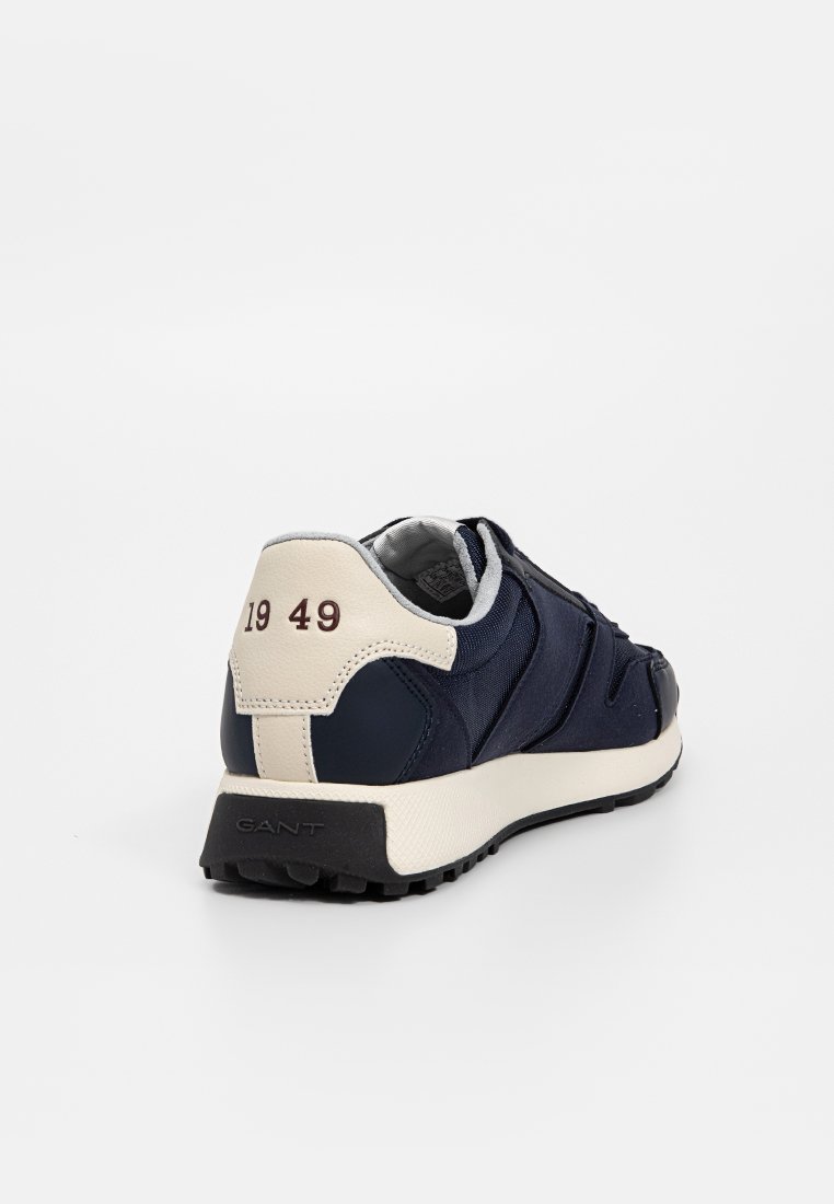 Navyblaue Sneaker mit einem strukturierten Textilobermaterial, cremfarbenem Absatz, schwarzer Gummisohle und "1949" auf der Rückseite aufgedruckt.
