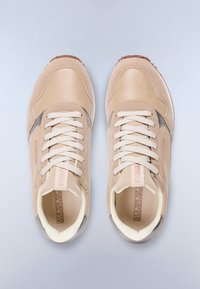 Un paio di sneakers beige con lacci, colli imbottiti e suole in gomma, viste dall'alto su uno sfondo grigio chiaro.
