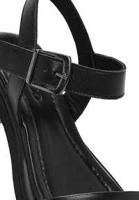 Sandalias de tacón alto de cuero negro con tira en el tobillo, que cuentan con una hebilla metálica y una textura suave y brillante en la parte superior y la suela interior.
