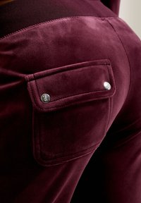 Bordeaux velours broek met een gladde textuur, voorzien van een achterzak met zilverkleurige hardware en een contrasterende tailleband.