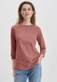 Maglia a maniche lunghe rosa polveroso con scollo rotondo, maniche raglan e texture morbida, abbinata a jeans di denim azzurri.